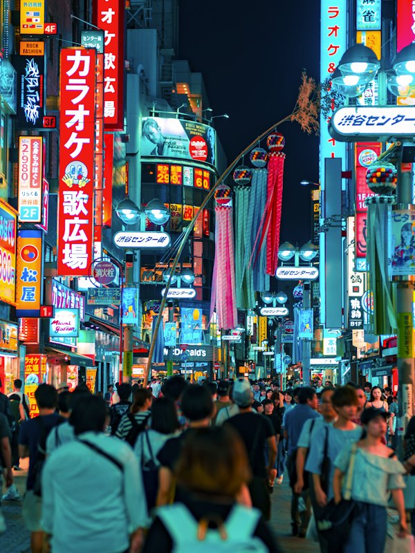 A crowd walking down a neon-lit street in Shibuya, Tokyo